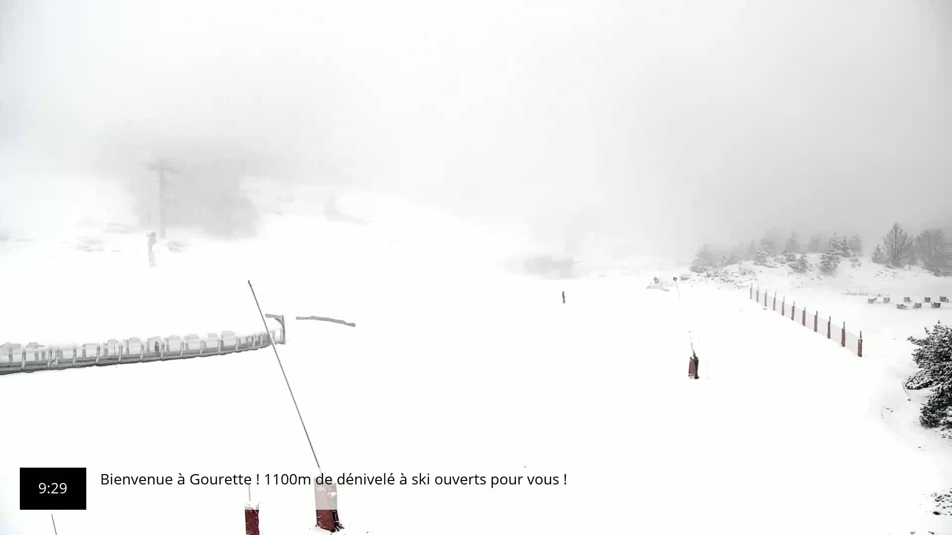 A snow-covered ski slope is visible in heavy snow, with a ski lift and snow fencing in the foreground.