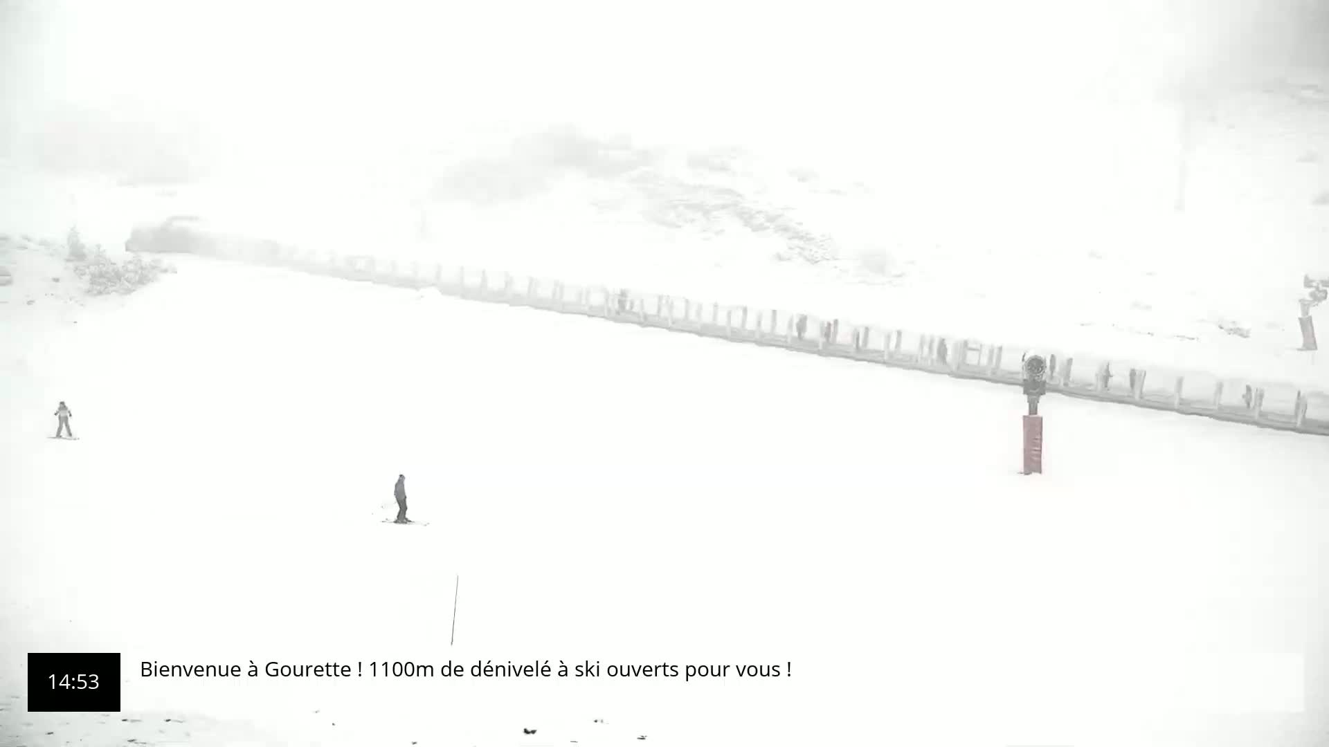 Two skiers are visible on a snow-covered slope during a heavy snowstorm.
