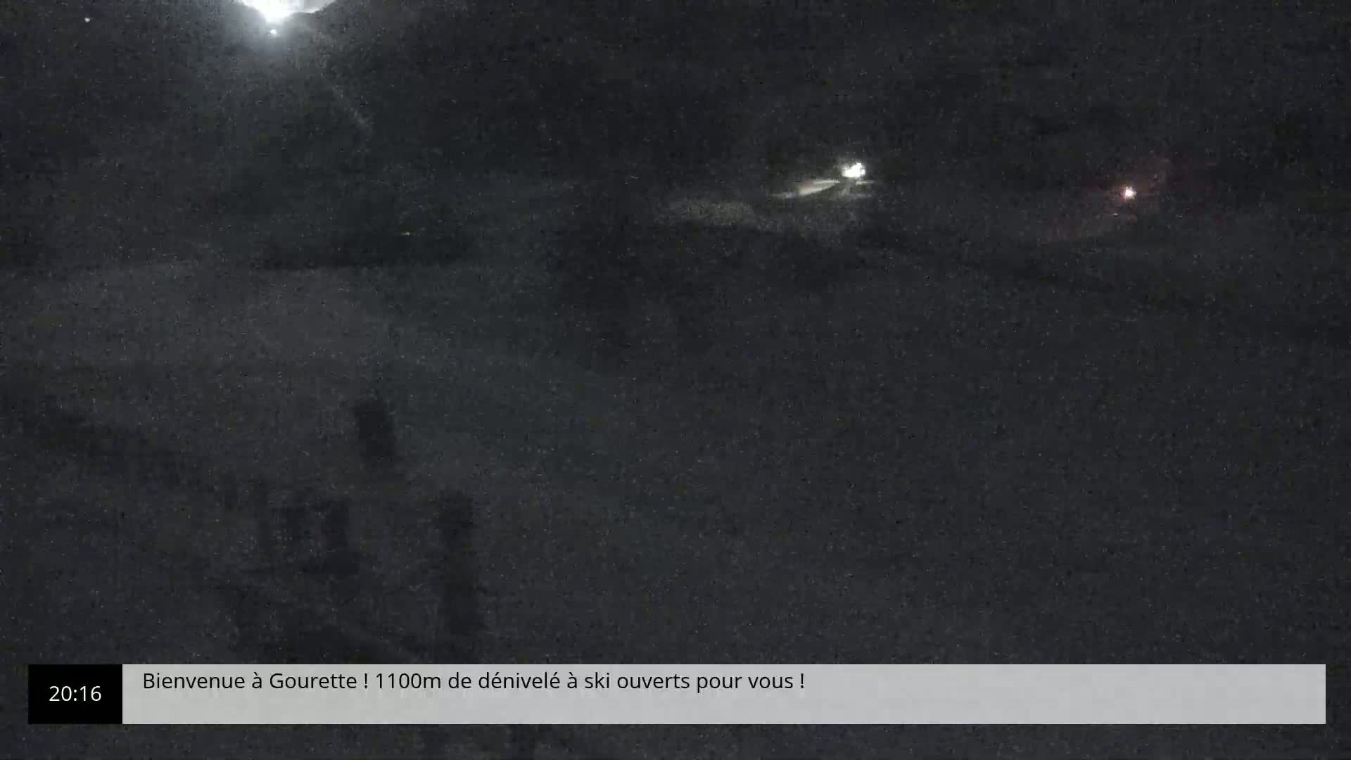 A nighttime, snowy scene shows a dark road with a few distant lights.