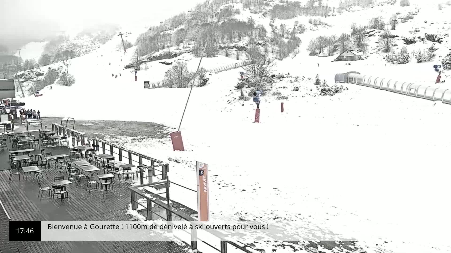 A snow-covered ski resort with a deck of tables and chairs overlooking a ski slope.