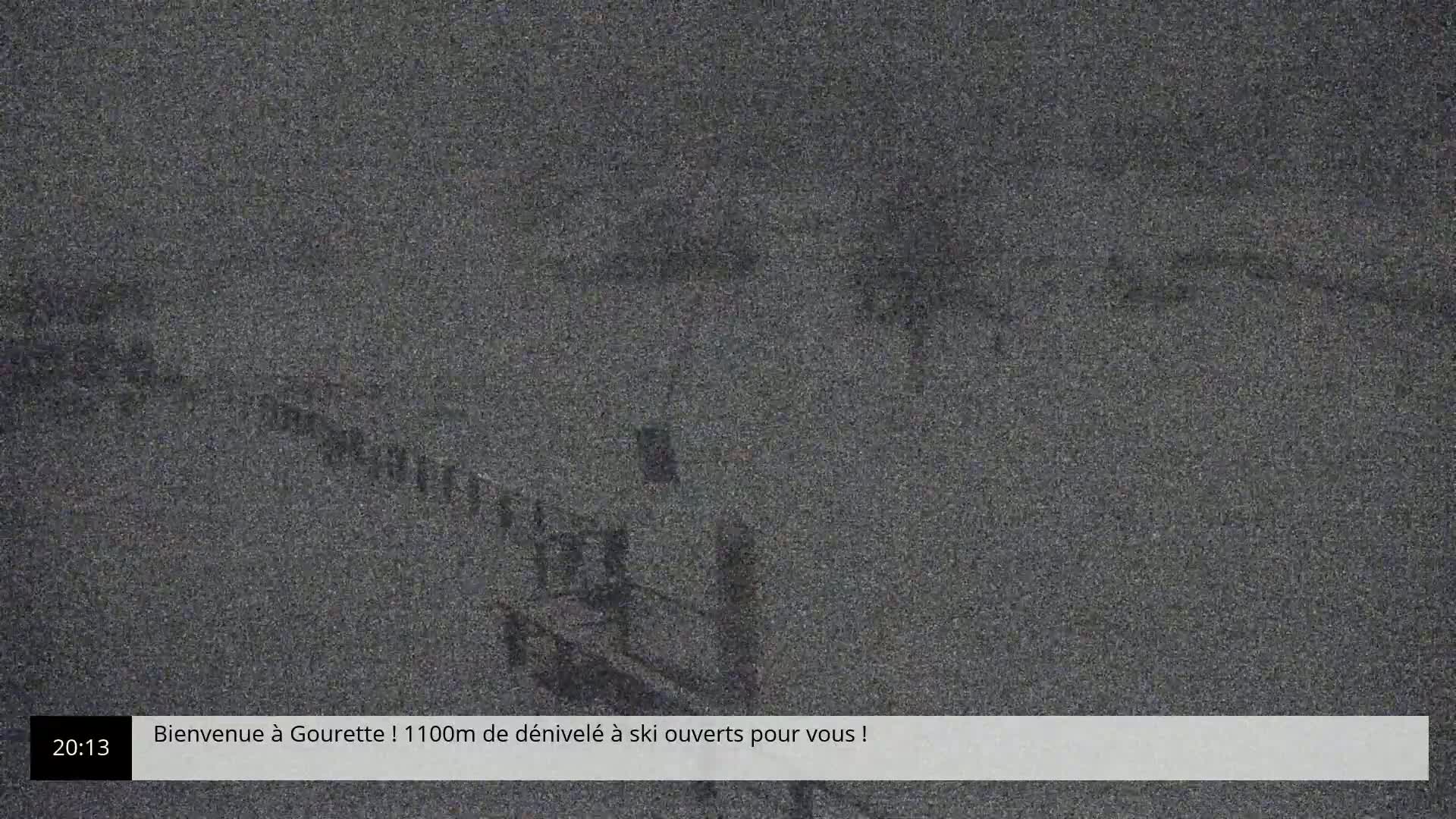 A nighttime, snowy scene shows a blurry, indistinct view of a landscape with some structures partially visible.