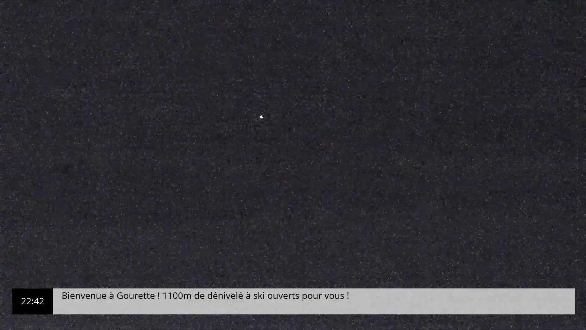 A dark, possibly nighttime image shows a single, faint light source in the center against a grainy, black background.