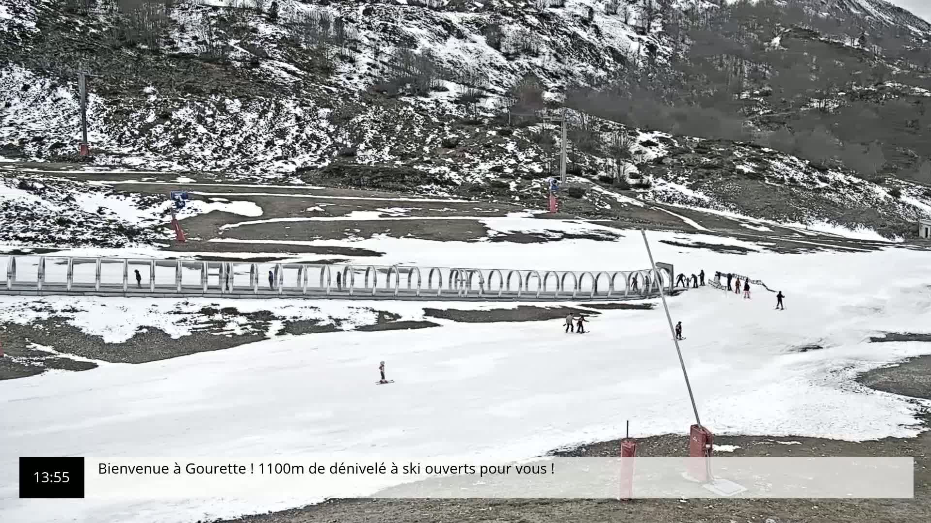 A snowy ski slope with a few skiers and a mountainside in the background.