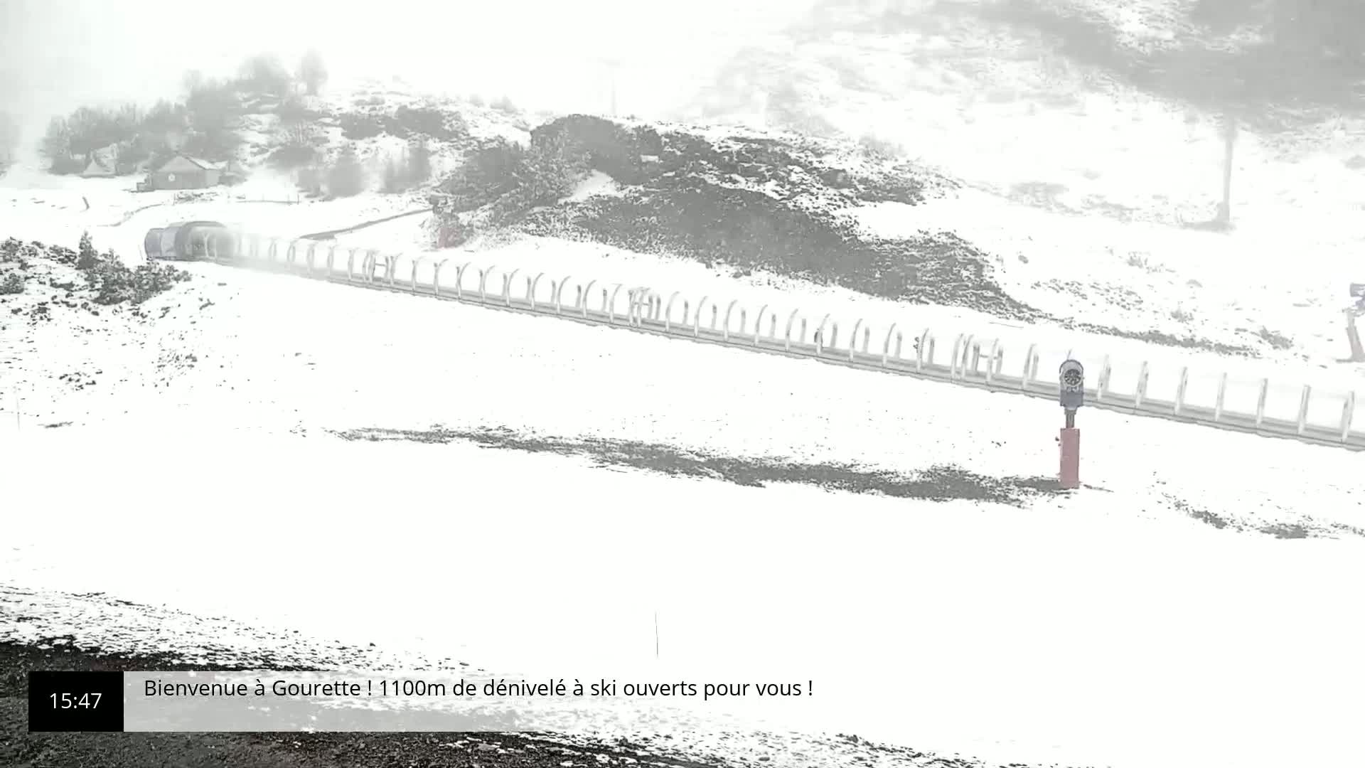 A snow-covered ski slope with a lift and a building in the distance during a heavy snowstorm.