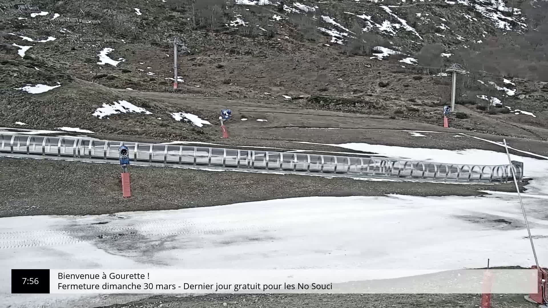 A snowmaking machine sits near a partially snow-covered, sloped area with a curved, transparent enclosure.