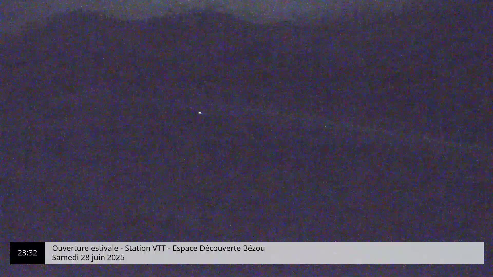 A dark, nighttime view of a distant, blurry landscape under a clear sky with a single, faint light visible in the distance.