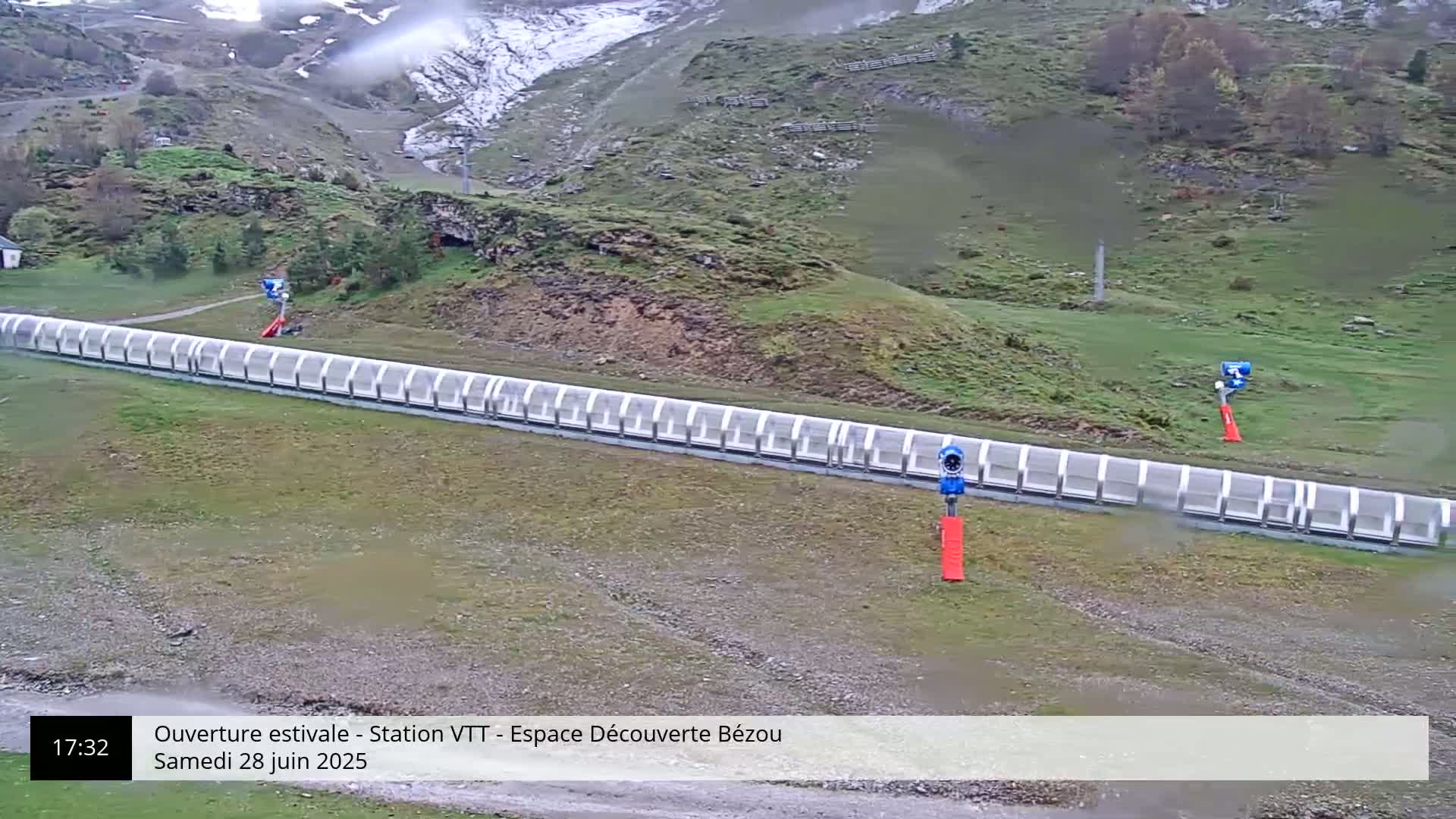 A long, covered track runs horizontally across a grassy hillside in overcast conditions, with small structures at either end.