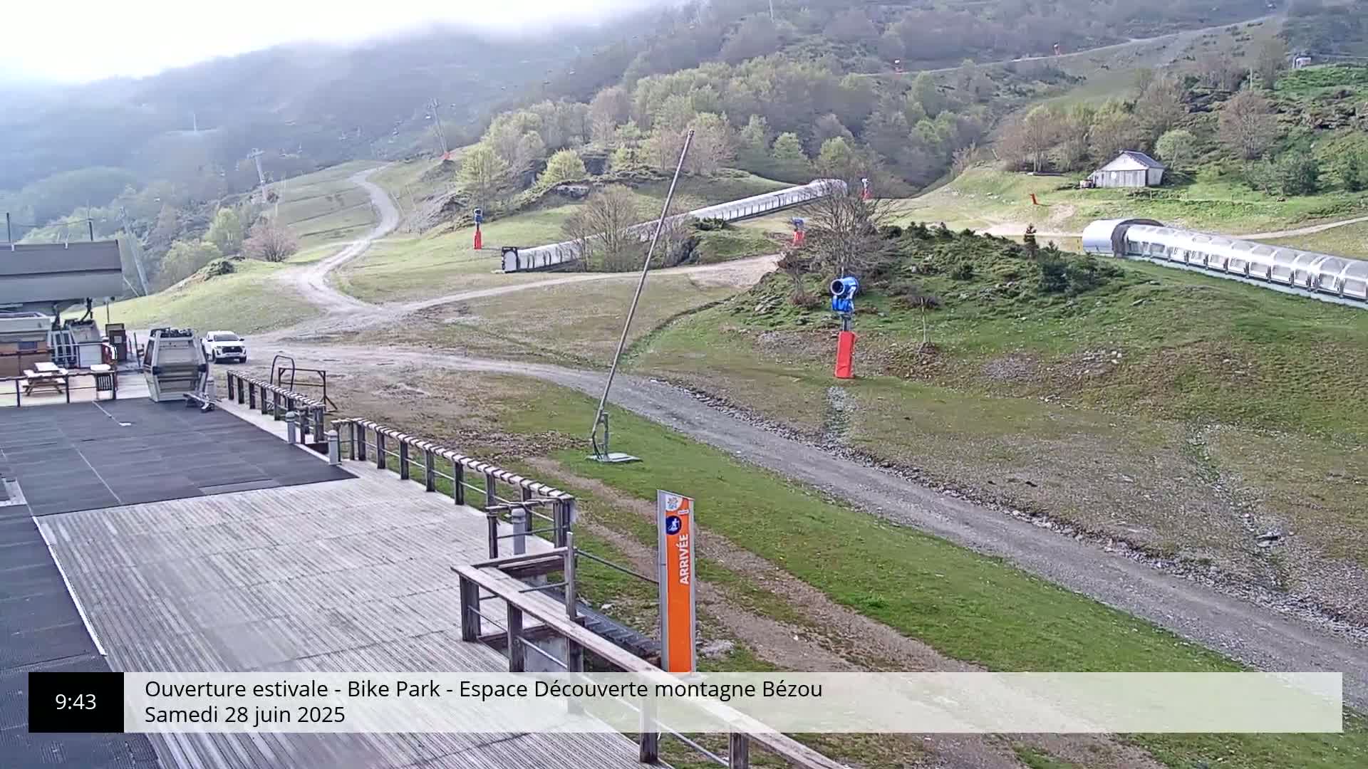 An overcast mountaintop bike park with a paved area, a dirt road, and several covered conveyor belts.