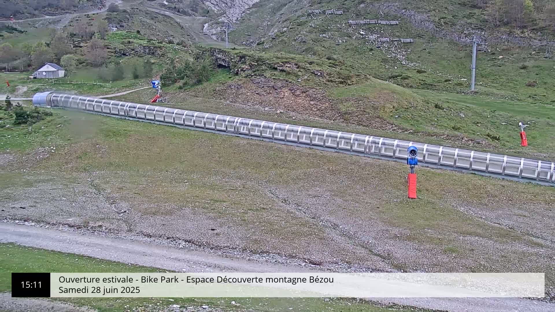 A long, covered track runs horizontally across a mountainous, grassy area under a mostly clear sky.