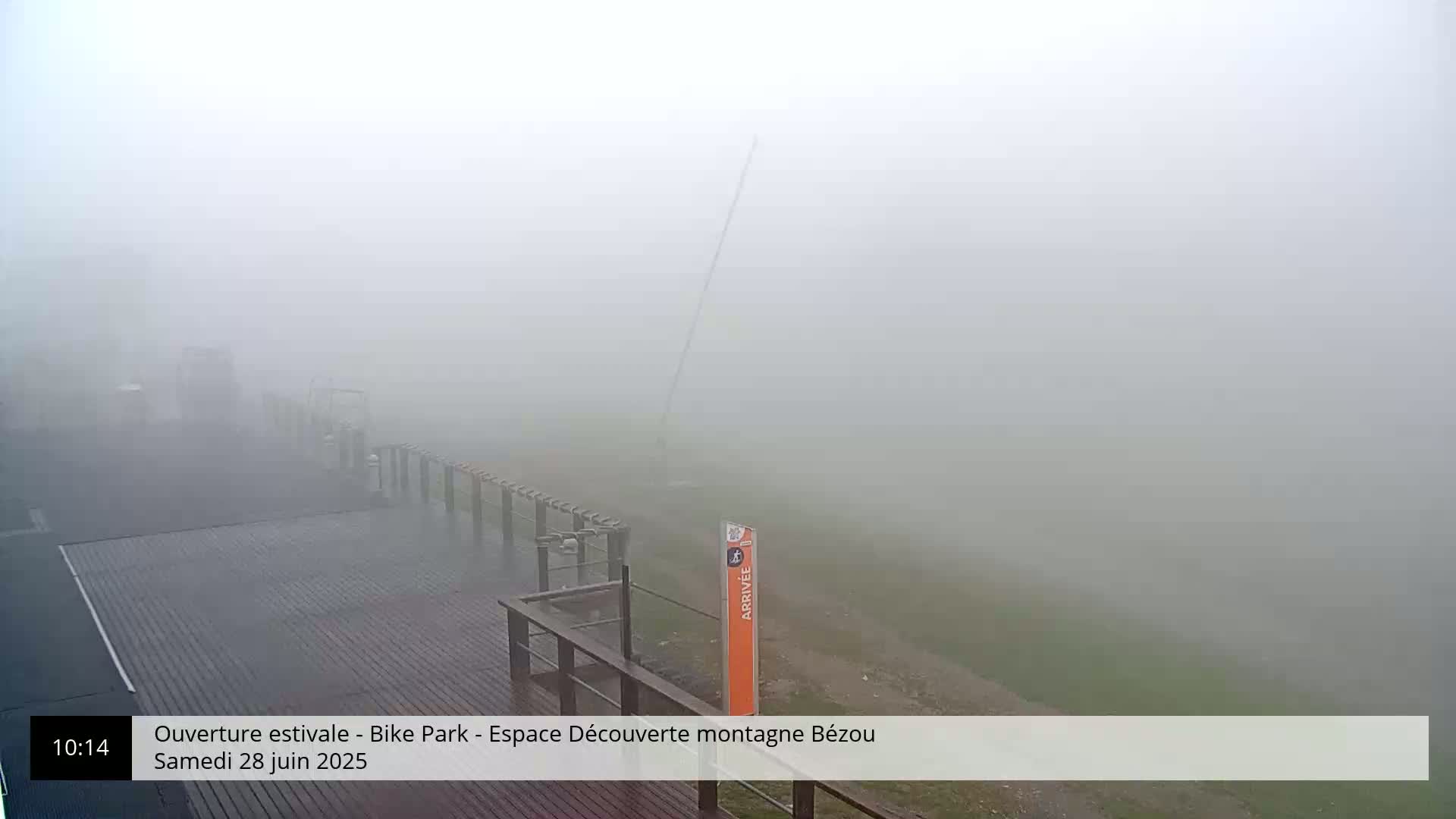 A foggy outdoor scene shows a wooden deck and railing with a tall pole in the mid-ground, all partially obscured by heavy fog.