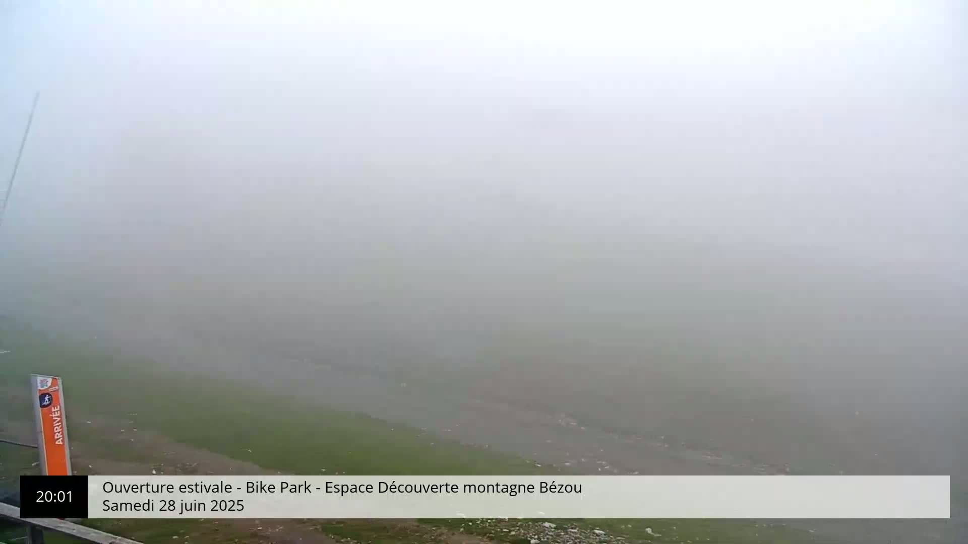 A foggy, outdoor scene shows a grassy field and a road partially obscured by thick fog.