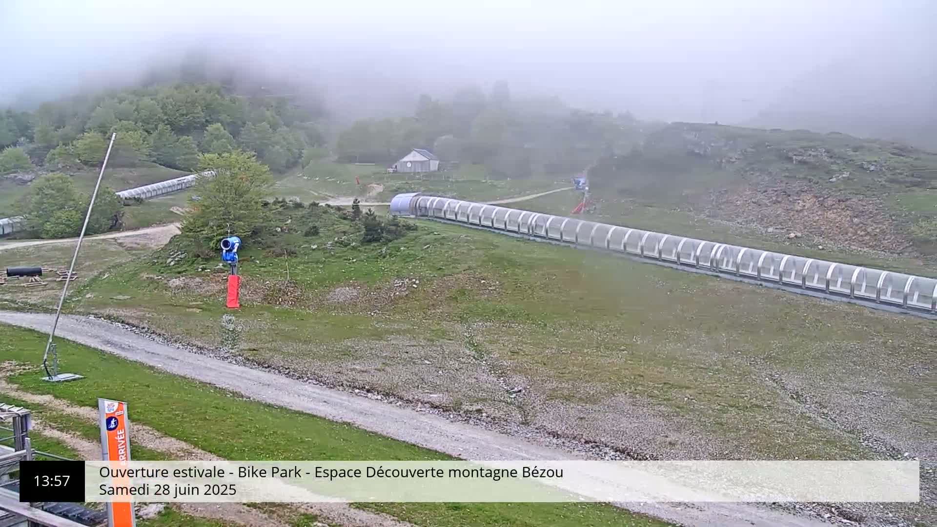 A foggy mountain bike park with a long covered lift and a snow-making machine is visible from a high vantage point.
