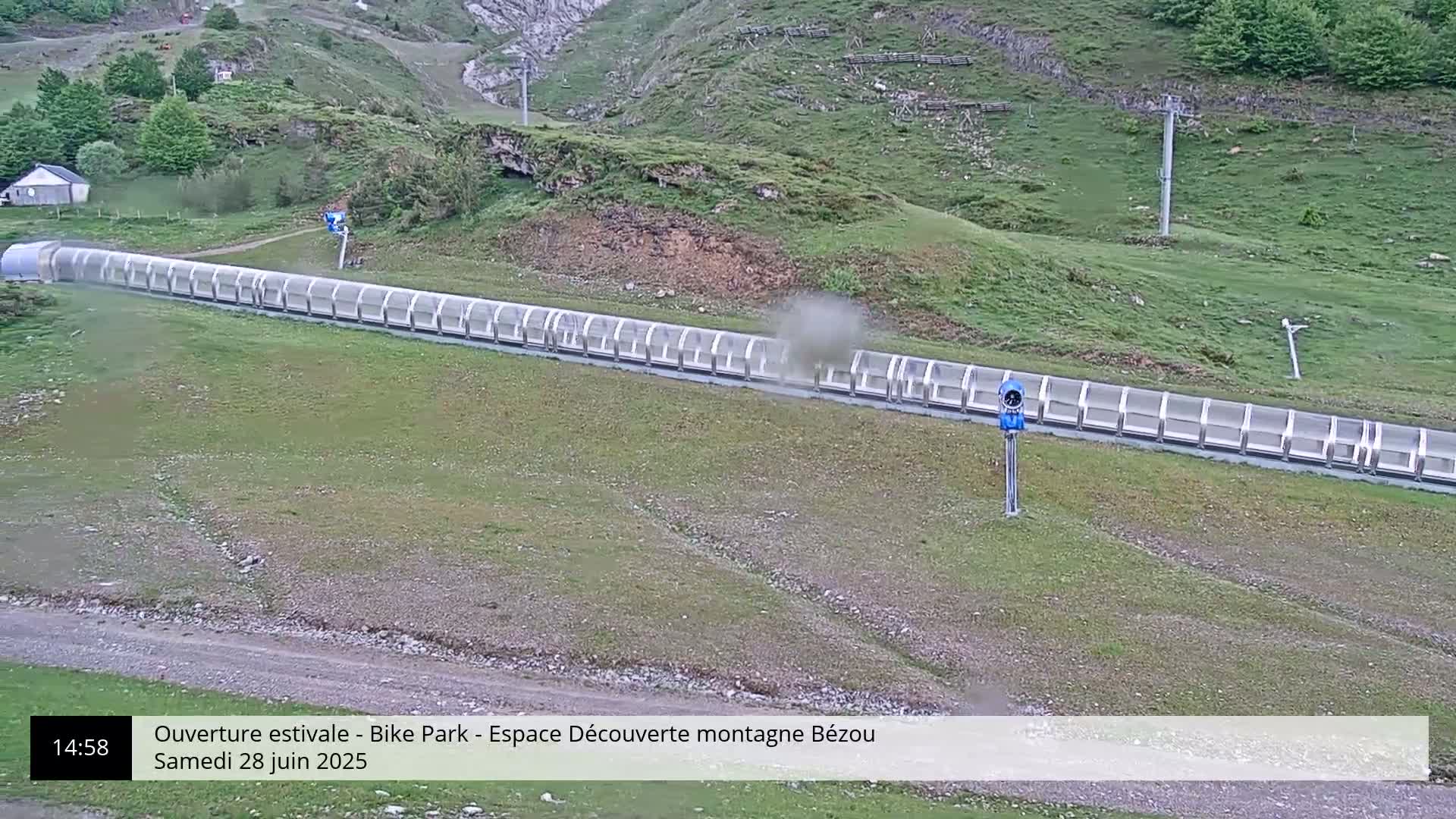 A long, covered uphill conveyor belt system sits on a grassy hillside, with a small cloud of dust rising from it.