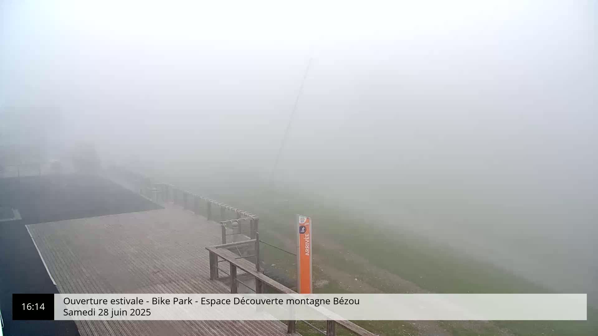 A wooden deck overlooks a foggy, grassy area with a tall structure in the distance.