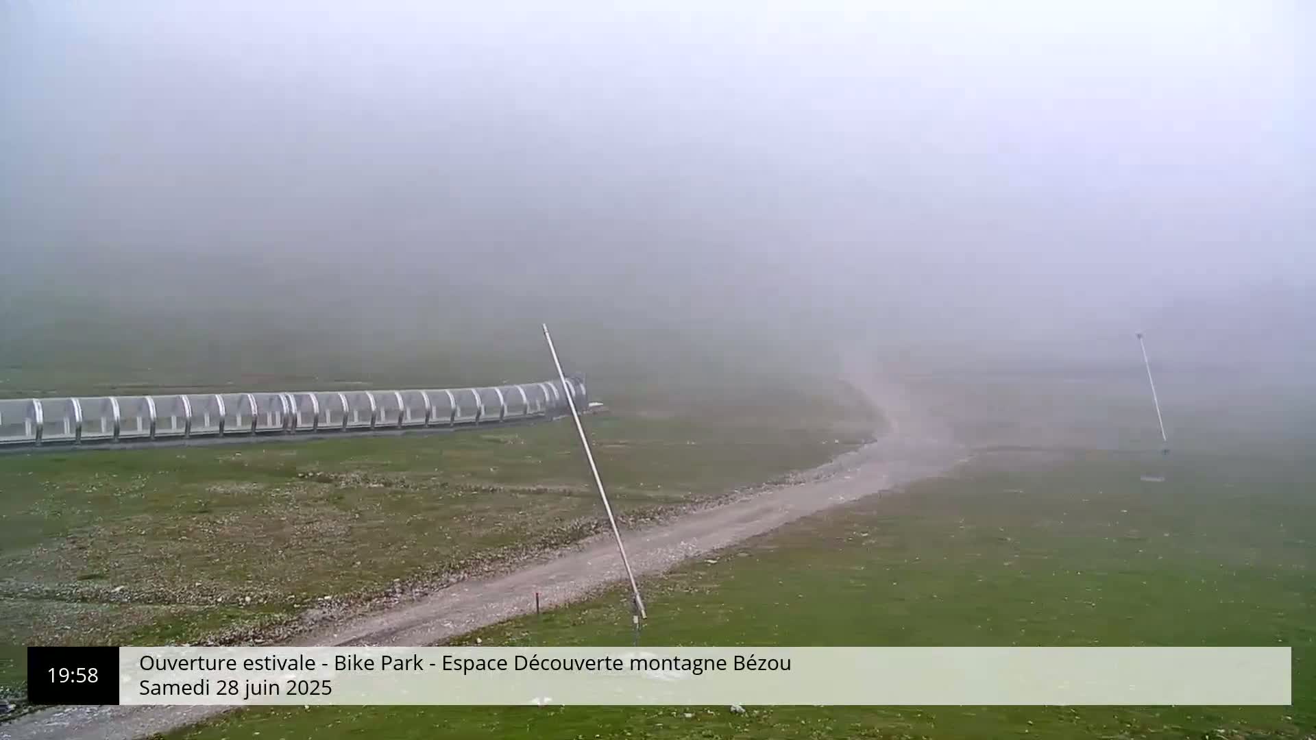 A long, covered structure sits in a grassy field on a foggy day.