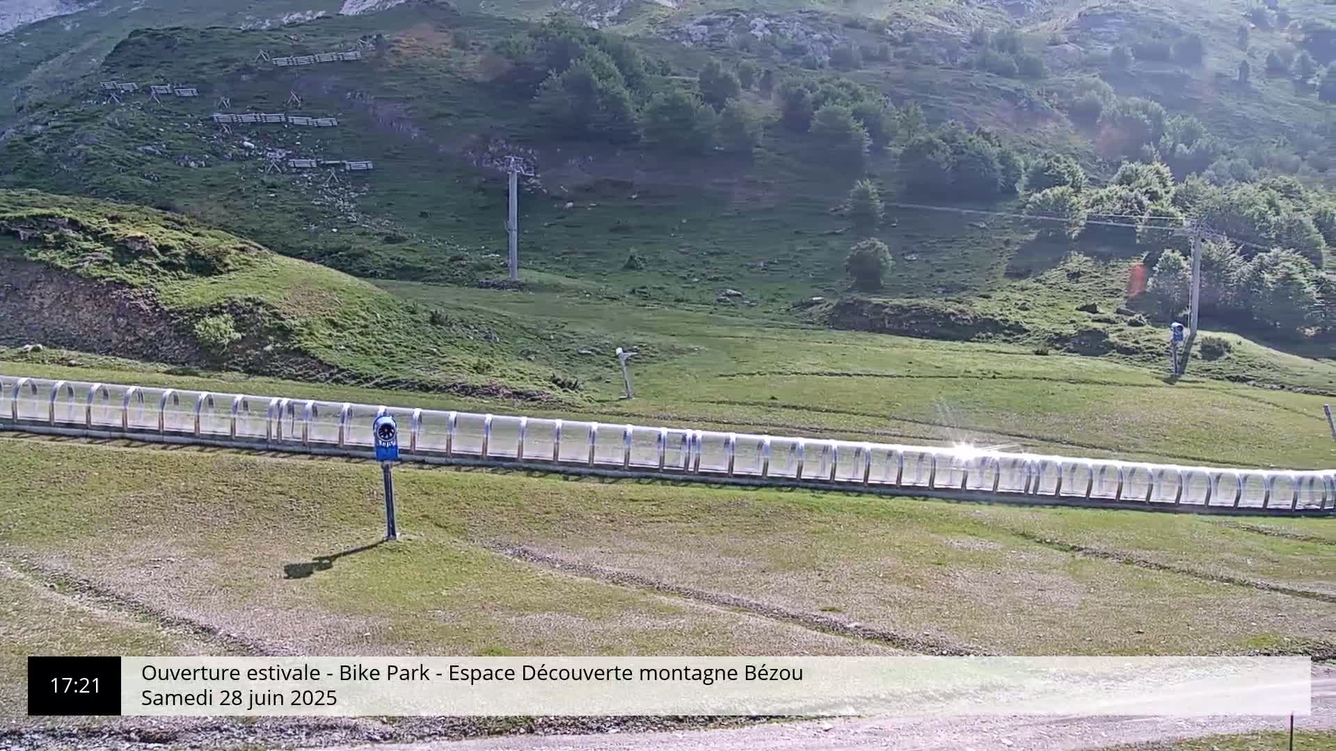 A long, covered track extends across a grassy hillside under a sunny sky.
