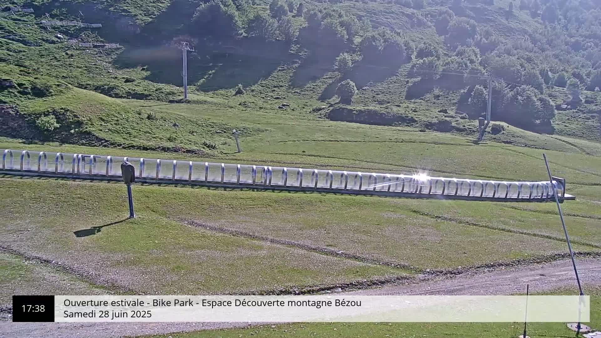 A long, covered track sits on a grassy hillside under a sunny sky.