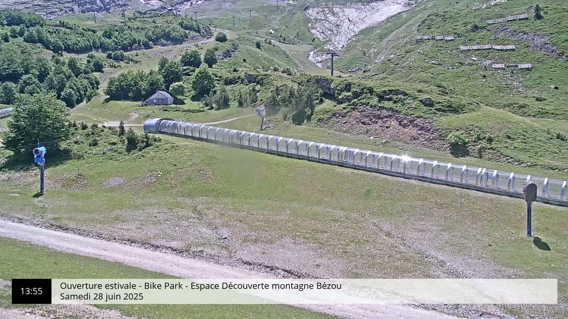 A long, covered track sits on a grassy hillside under a sunny sky.