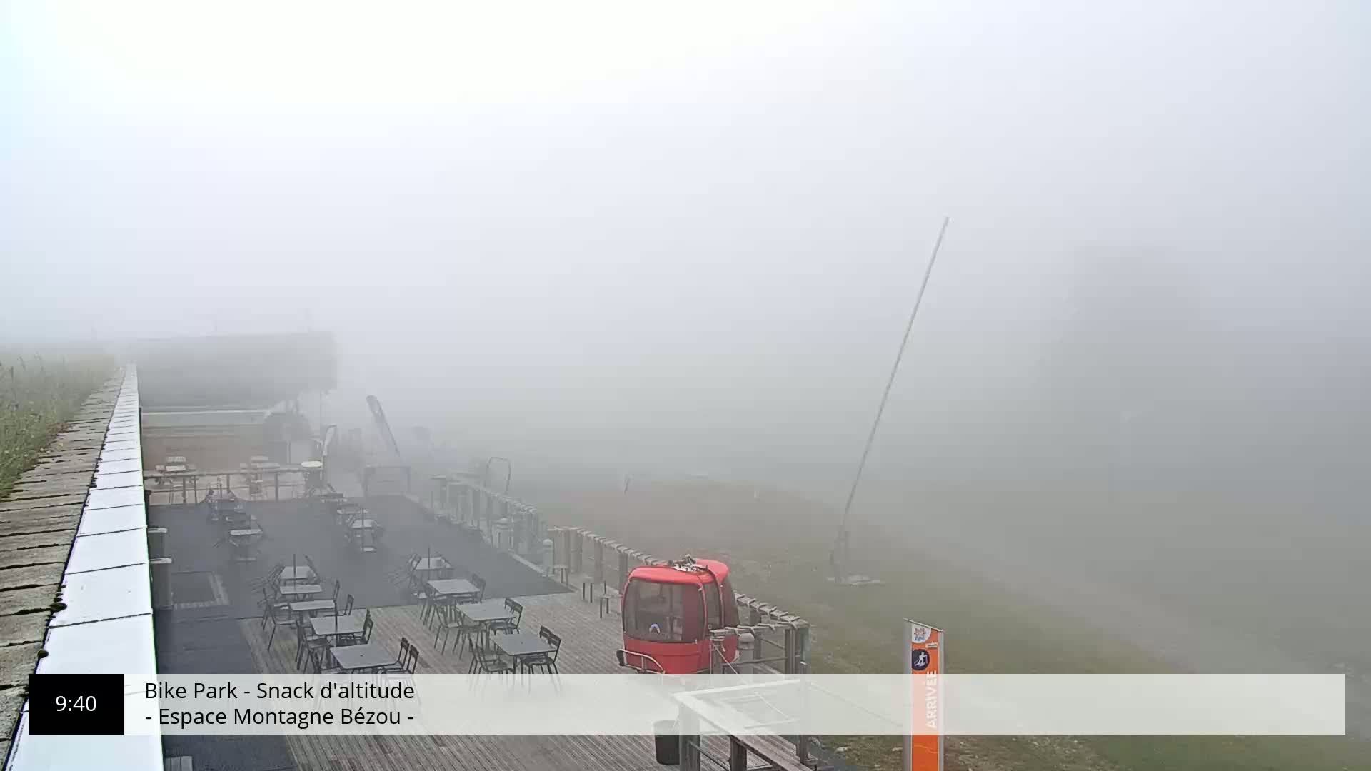 A foggy outdoor scene shows an empty outdoor cafe area with a red cable car, and a long cable stretching into the thick fog.