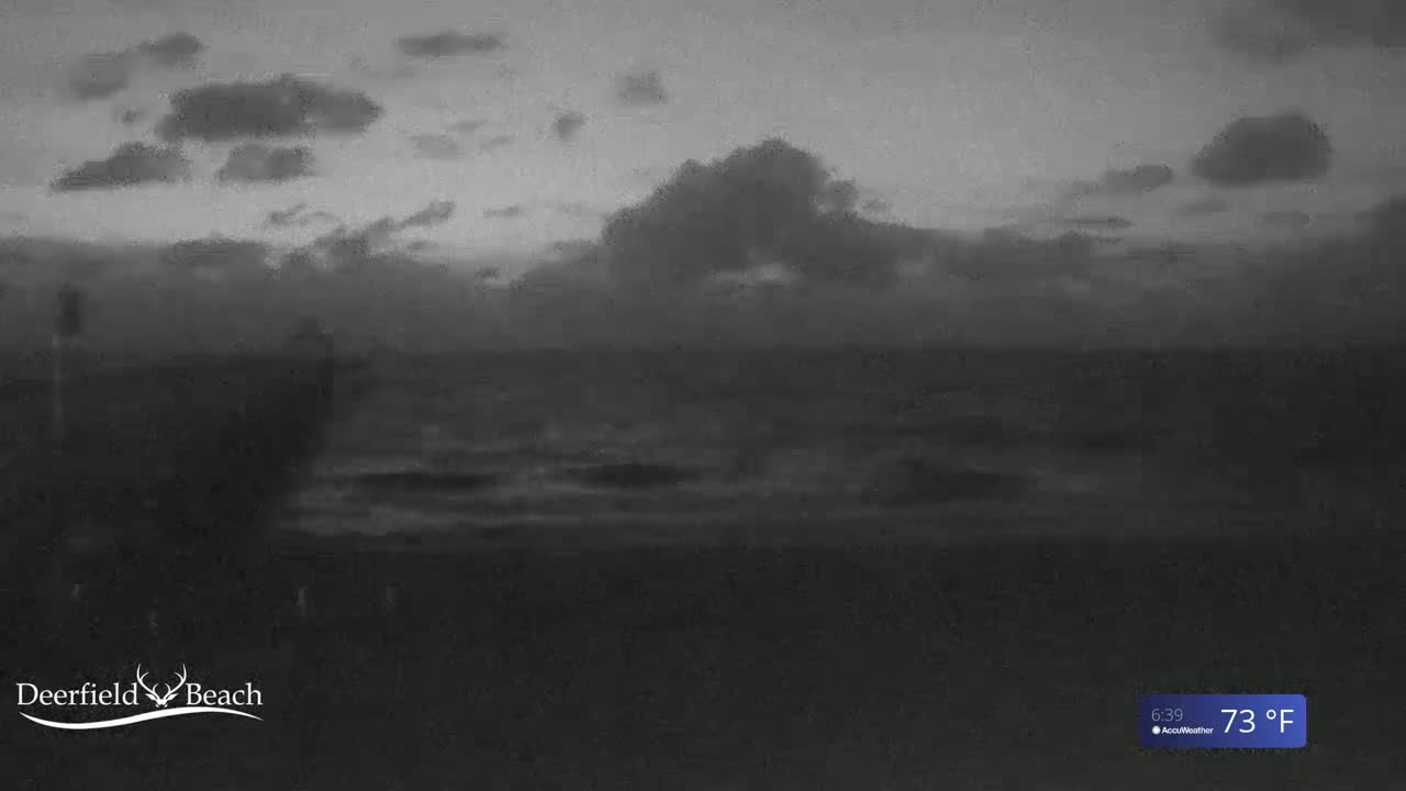 A dark, cloudy sky hangs over a calm ocean at night.