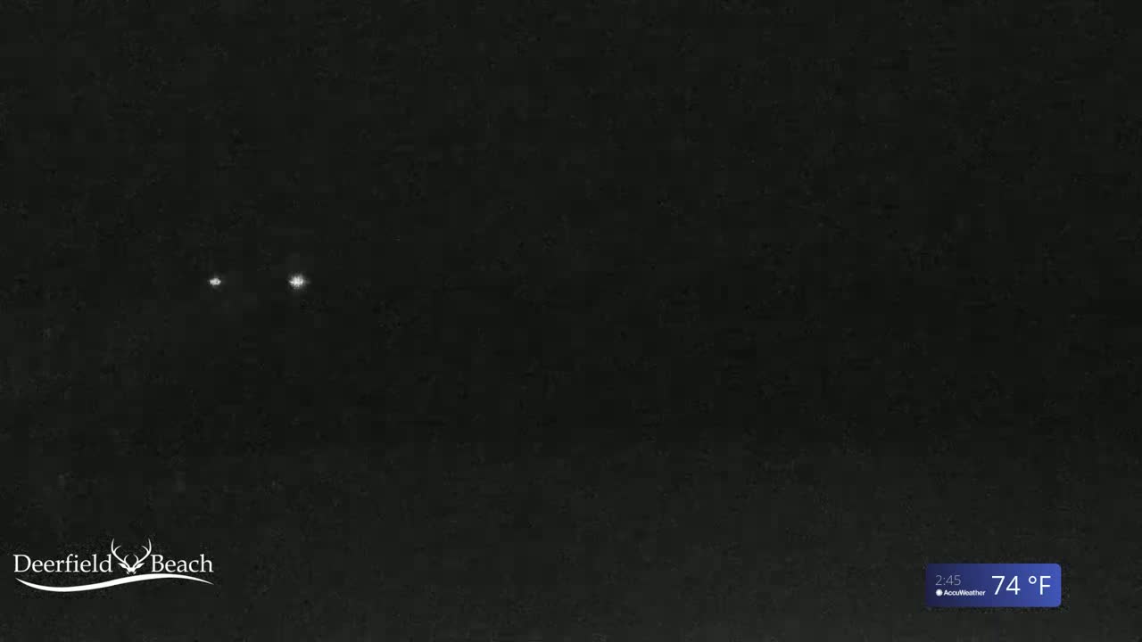 A nighttime image shows a dark, possibly sandy, area with two faint lights in the distance under a clear sky at 74°F.