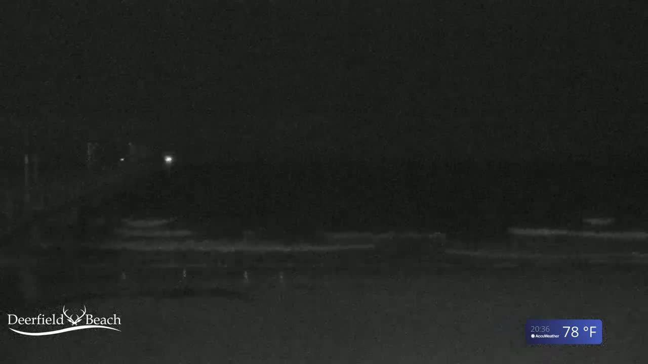 A nighttime, low-light view of a dark beach with a few faint lights visible in the distance, the temperature is 78°F.
