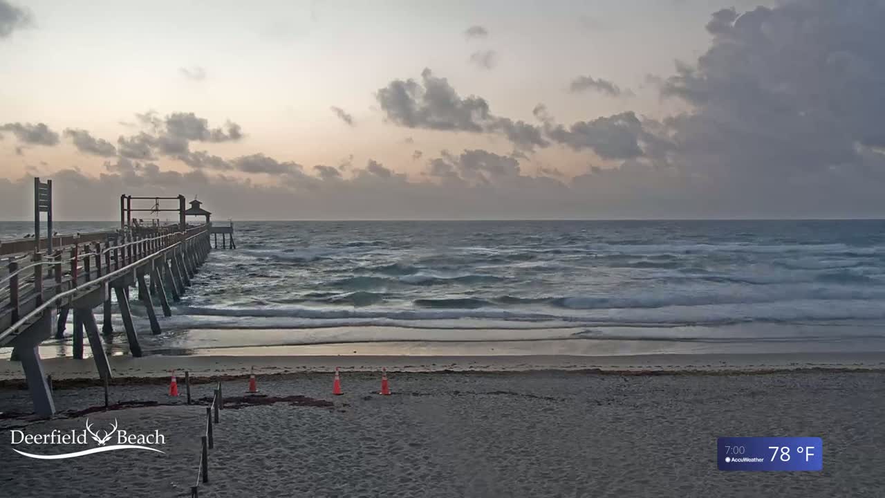 A long pier extends over a mostly calm ocean under a cloudy, sunrise sky.