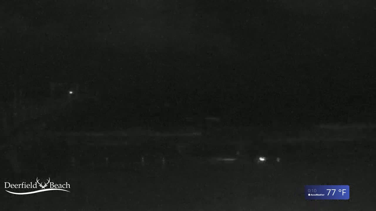A nighttime, low-light outdoor scene shows a dark road with a few faint lights and a dark horizon under a clear sky at 77°F.