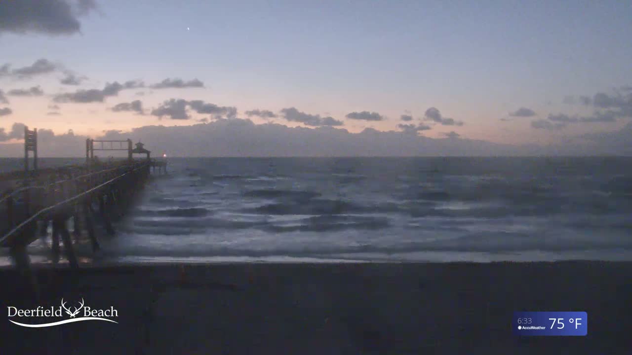 A long pier extends into a dark, choppy ocean under a dusky sky.