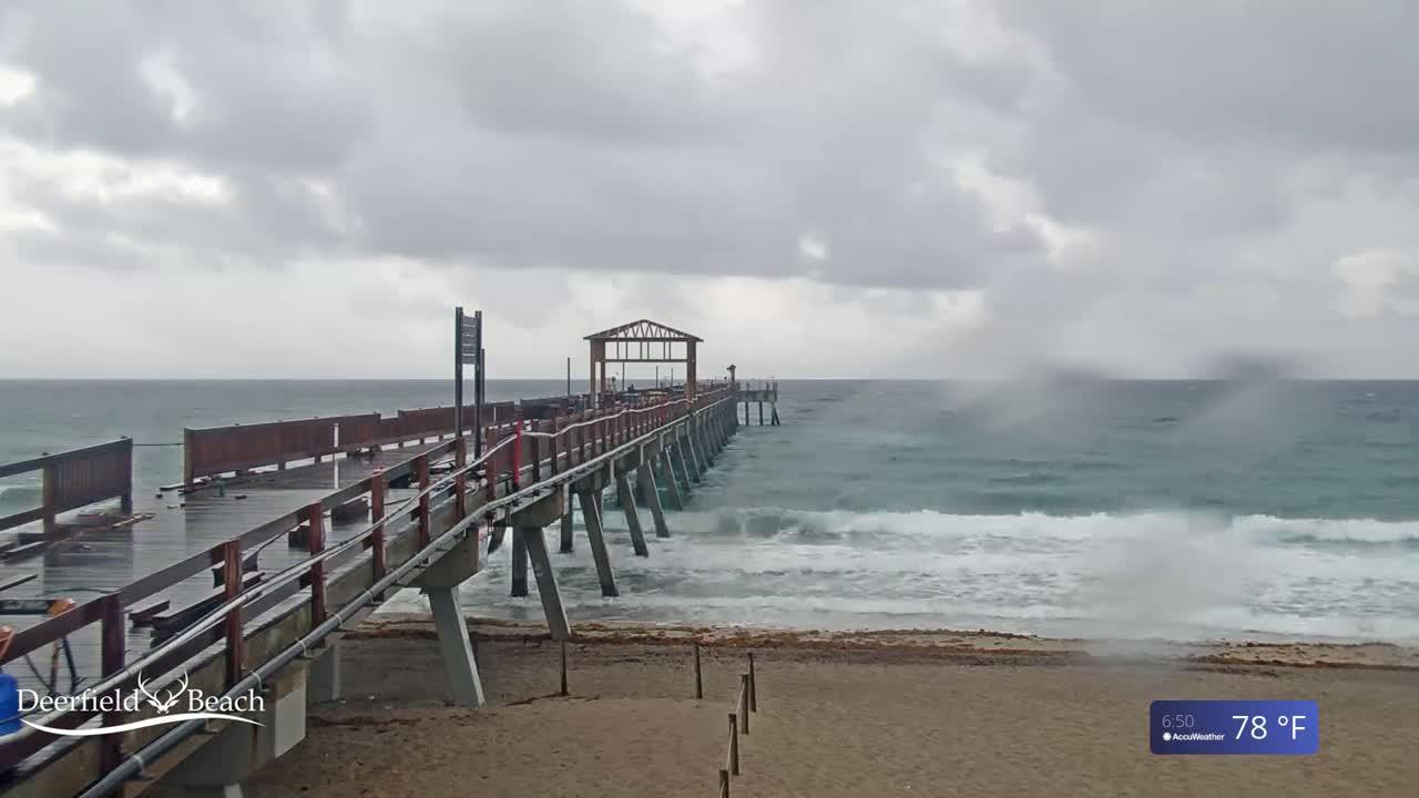 A long wooden pier extends into a choppy ocean under a cloudy sky.