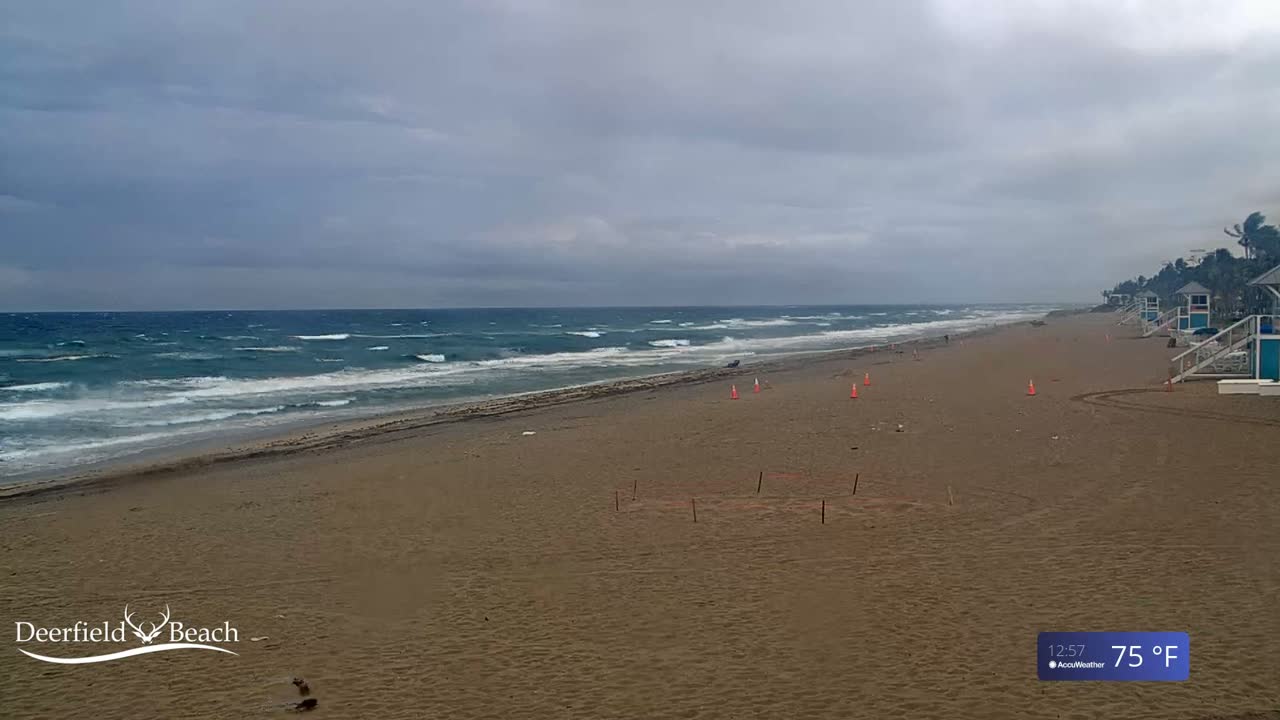 A mostly empty sandy beach with lifeguard stands and a choppy ocean under a cloudy sky.