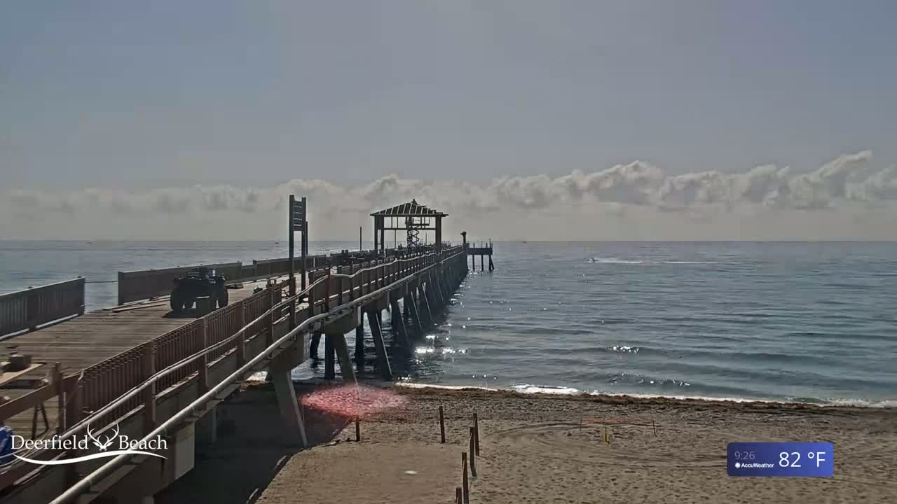 A long pier extends over a calm ocean under a partly cloudy sky, with a four-wheeler visible on the pier.