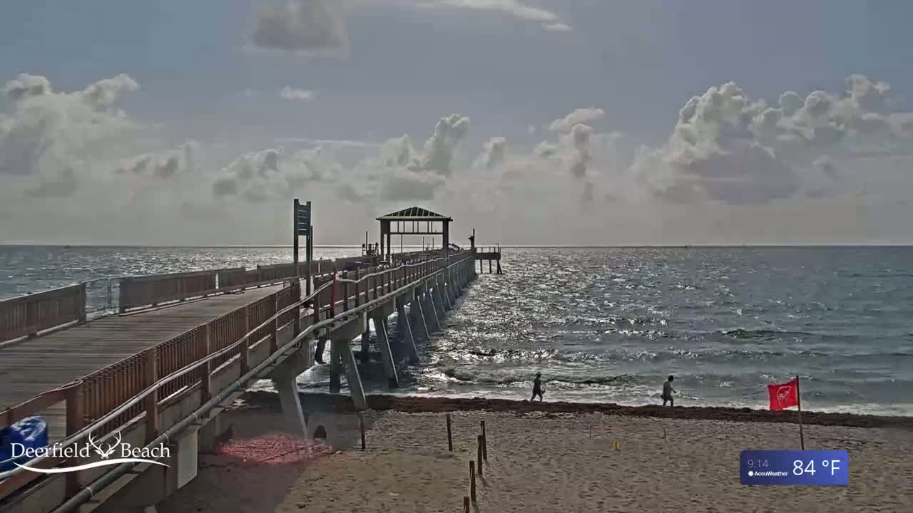 A long wooden pier extends over a somewhat choppy ocean under a partly cloudy sky.