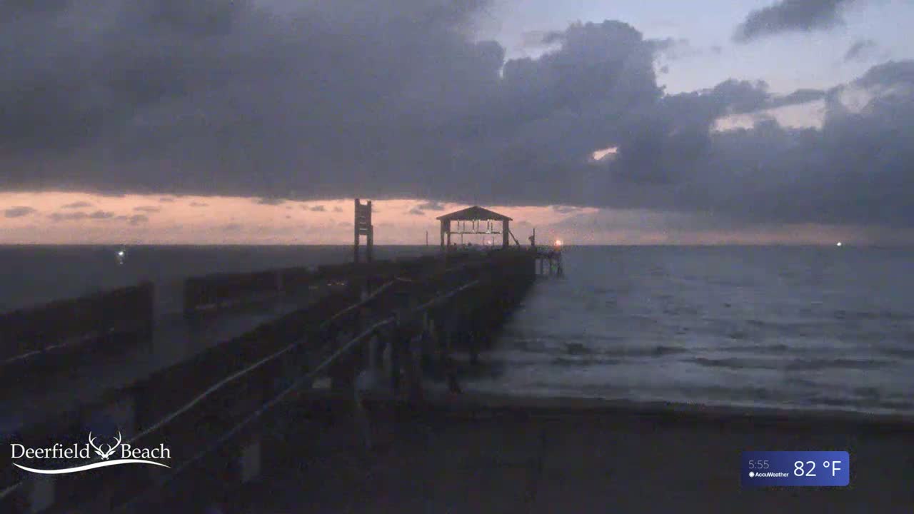 A long pier extends into a dark, somewhat choppy ocean under a cloudy, dusky sky.
