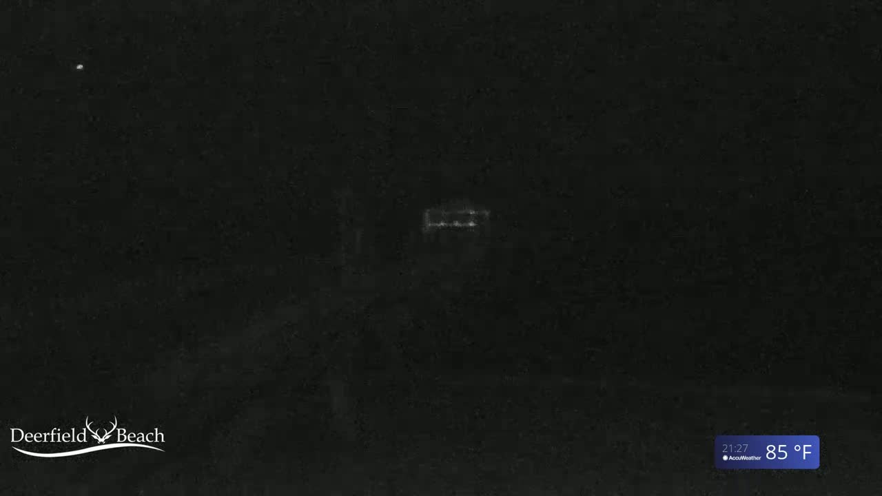 A dimly lit nighttime scene shows a structure with lights on in the distance under a dark sky.