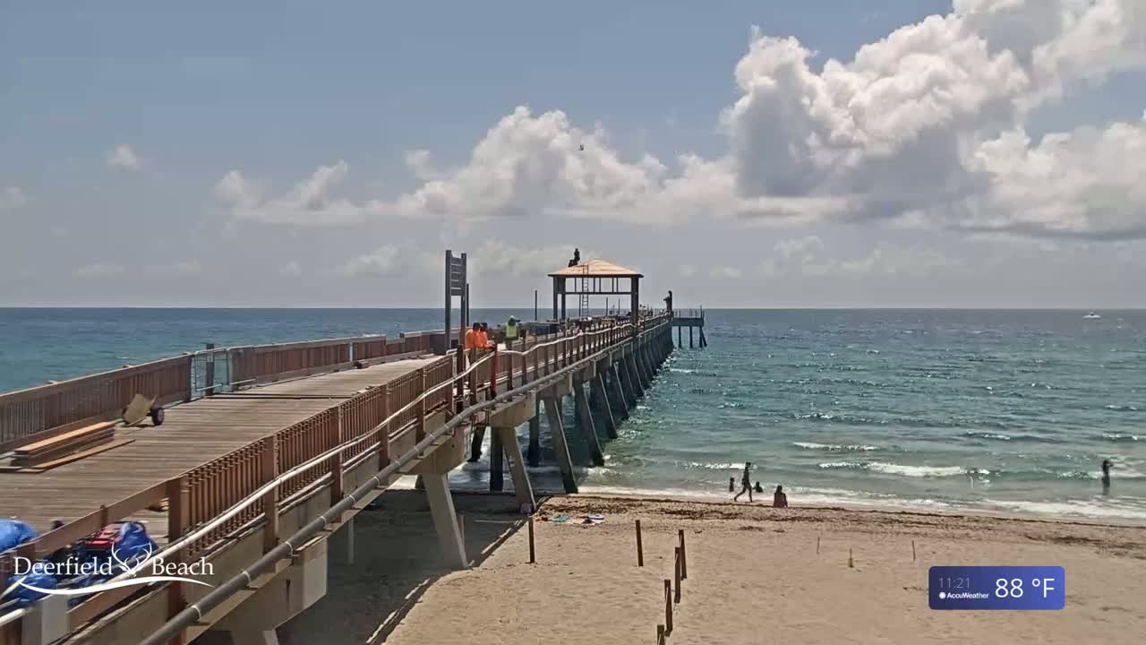 A partly cloudy day with 88°F weather shows a wooden pier extending over a calm ocean, with a few people on the beach and workers on the pier.