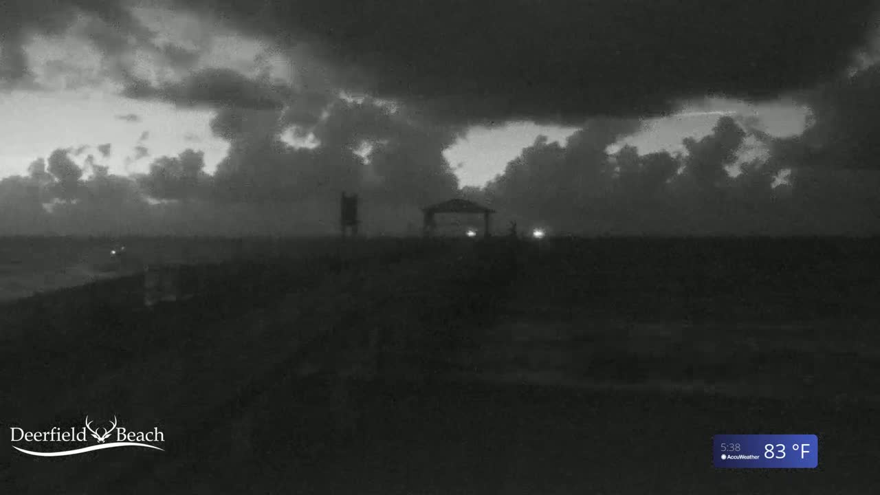 A dark, cloudy beach scene at night shows a gazebo and other structures silhouetted against a mostly overcast sky.