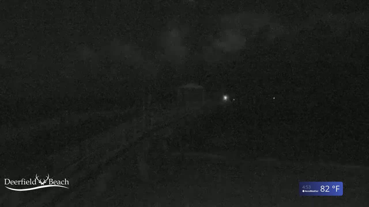A nighttime, low-light view of a dark, possibly wooded area with a few faint lights visible in the distance, under a cloudy sky, showing a temperature of 82°F.