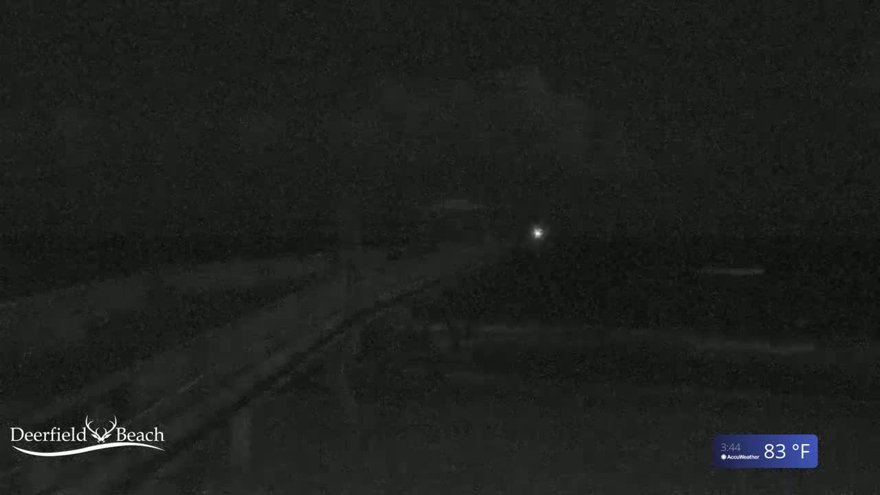 A dark, nighttime scene shows a dimly lit area, possibly a road or path, with a single, distant light source visible.