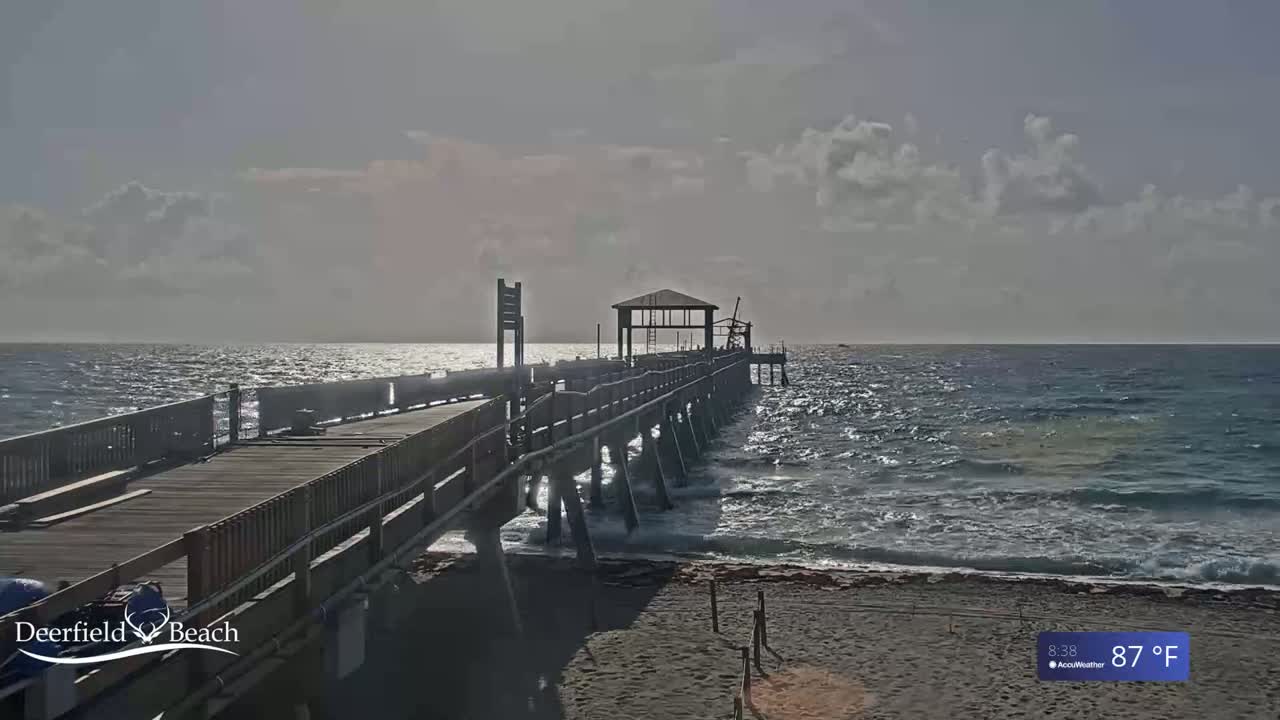A long pier extends over a gently wavy ocean under a partly cloudy sky.