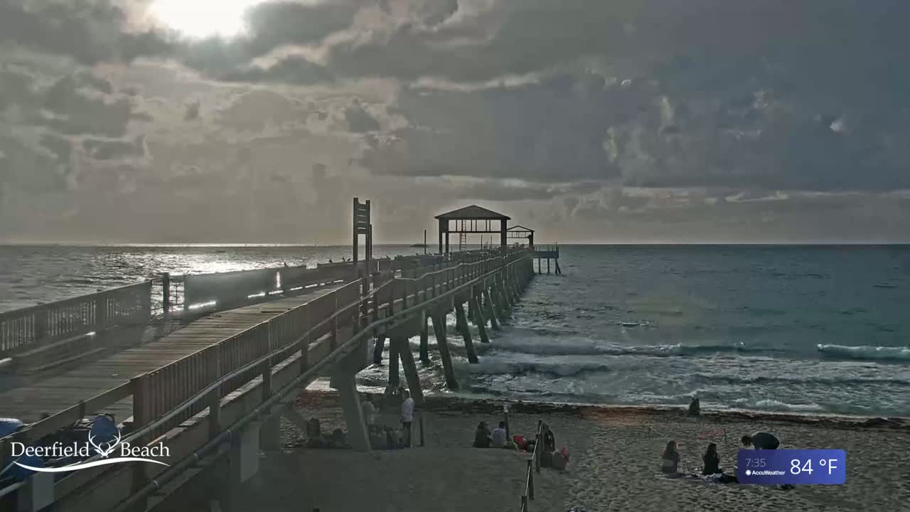 A long pier extends over a wavy ocean under a partly cloudy sky.