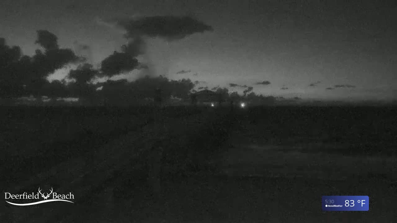 A dark, cloudy nighttime scene shows a flat, dark landscape with a few distant lights under a partly cloudy sky.