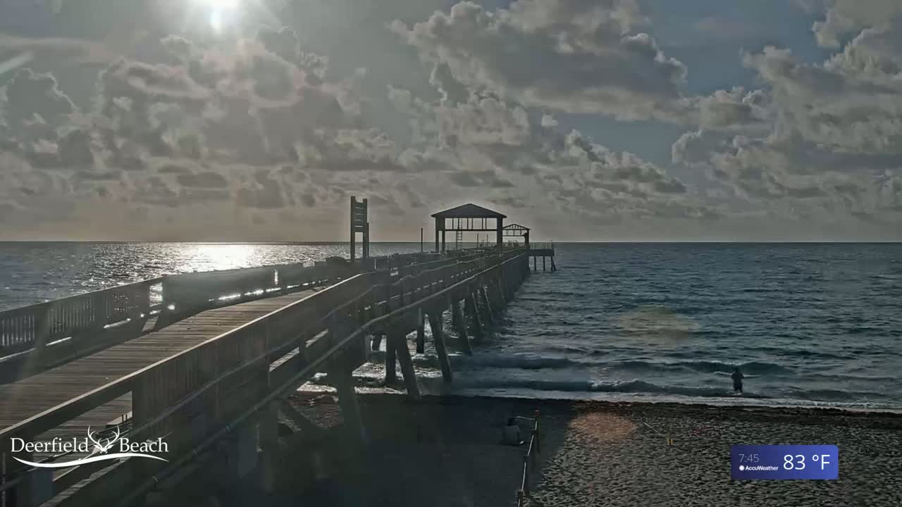 A long pier extends over a calm ocean under a partly cloudy sky.