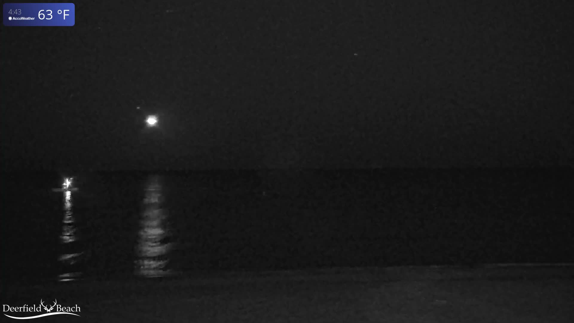 A dark night scene over calm water with clear skies features a bright light source on the left and a larger, more prominent light source in the upper right, both reflecting on the water's surface.