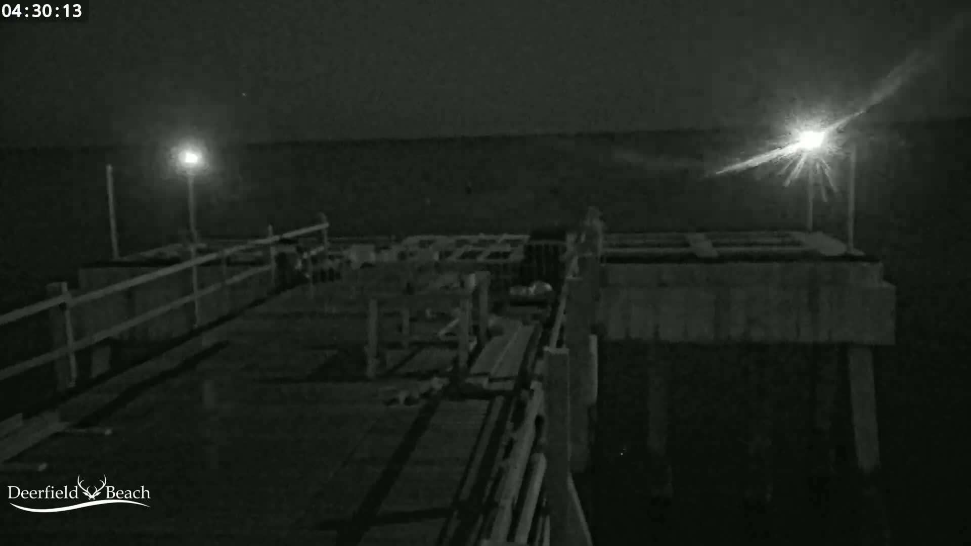 A nighttime, low-light image shows a section of a pier with lights illuminating the scene.