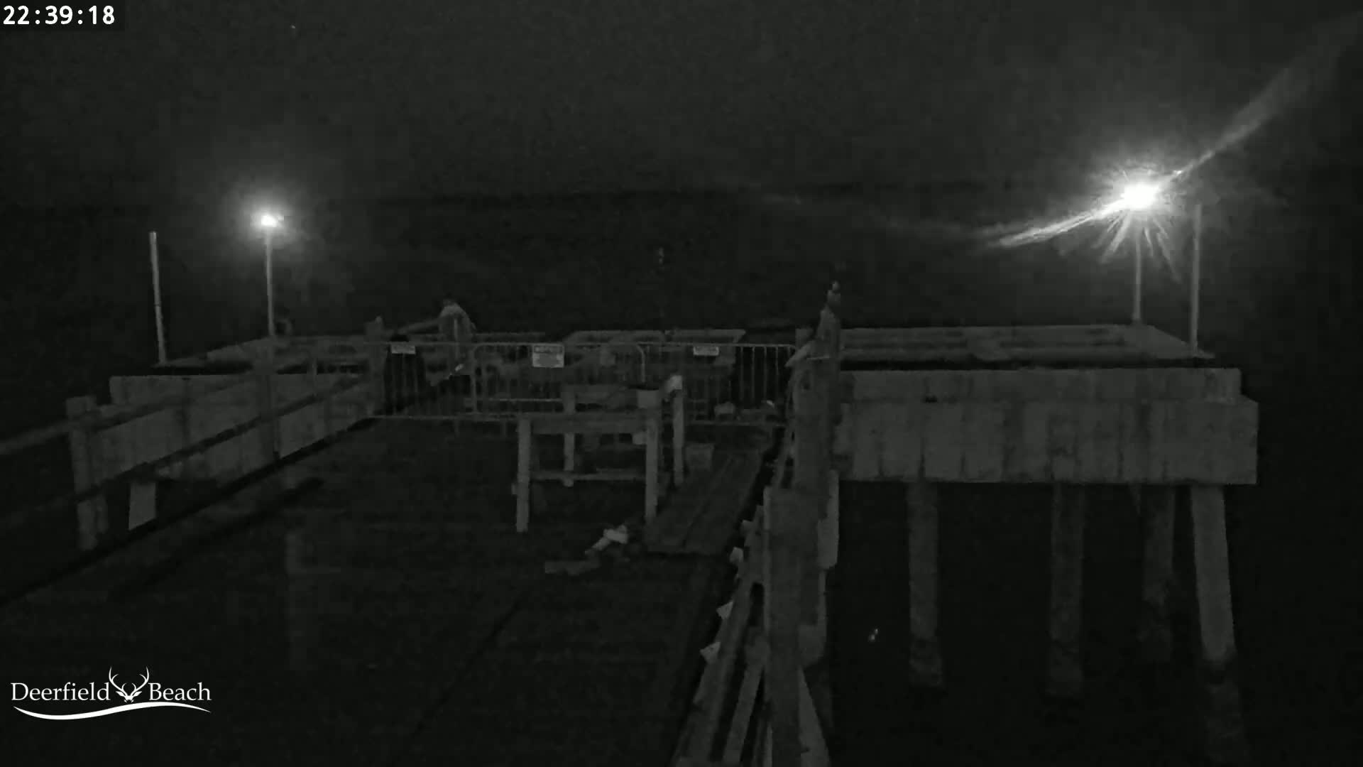A nighttime, low-light view of a pier with some people and barriers present.