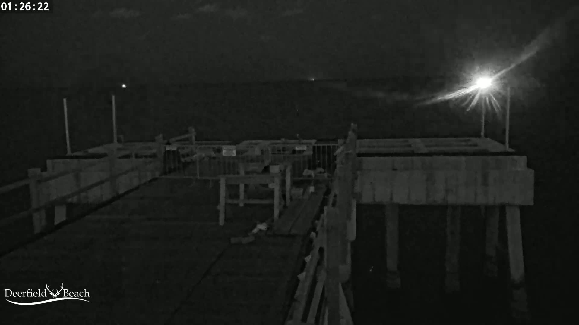 A nighttime view of a mostly empty pier extending over dark water under a partly cloudy sky.