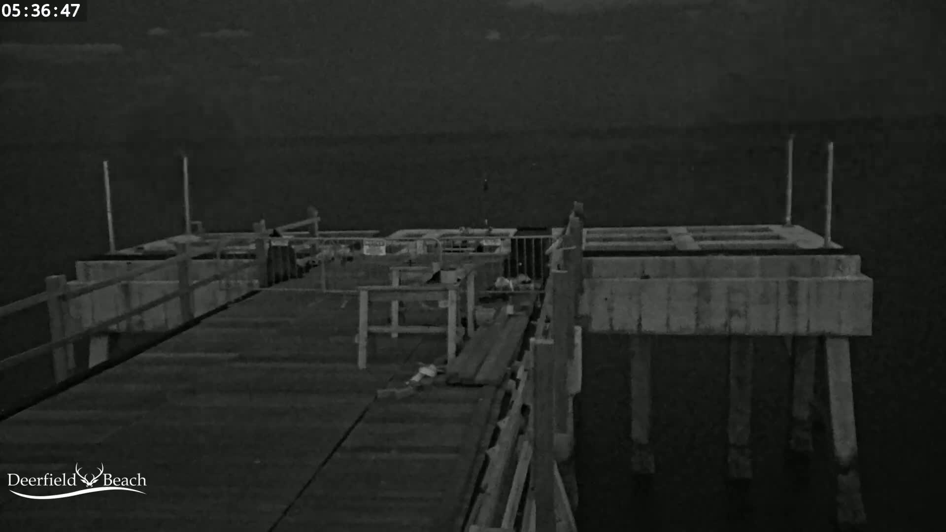 A nighttime, low-light view of a wooden pier extending over dark water.