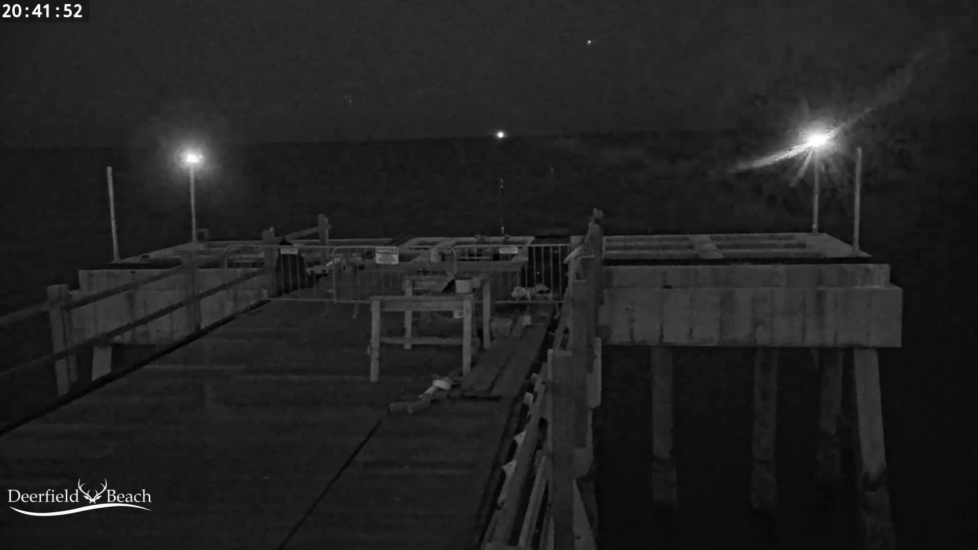 A nighttime, low-light view of a pier extending over dark water, illuminated by several bright lights.