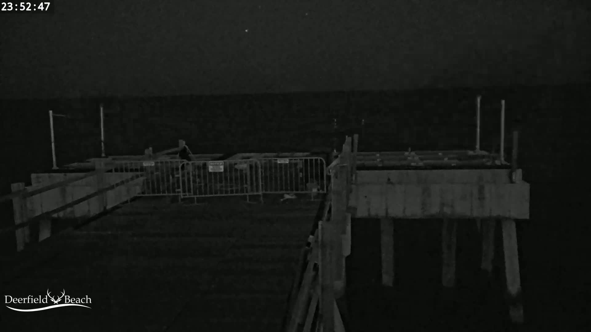 A nighttime, low-light image shows a section of a pier with metal barriers and concrete structures under a dark sky.
